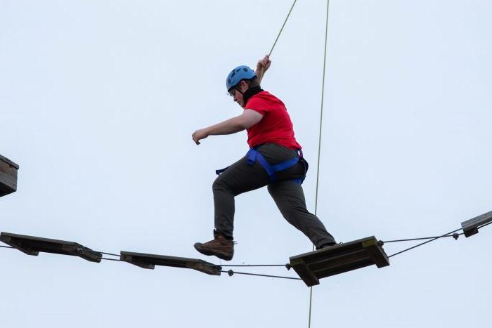 Person wearing red walking across logs on rope